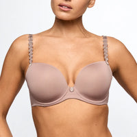A close-up of a model wearing a soft, muted pinkish-beige underwire bra with decorative silver coin-like embellishments along the straps.