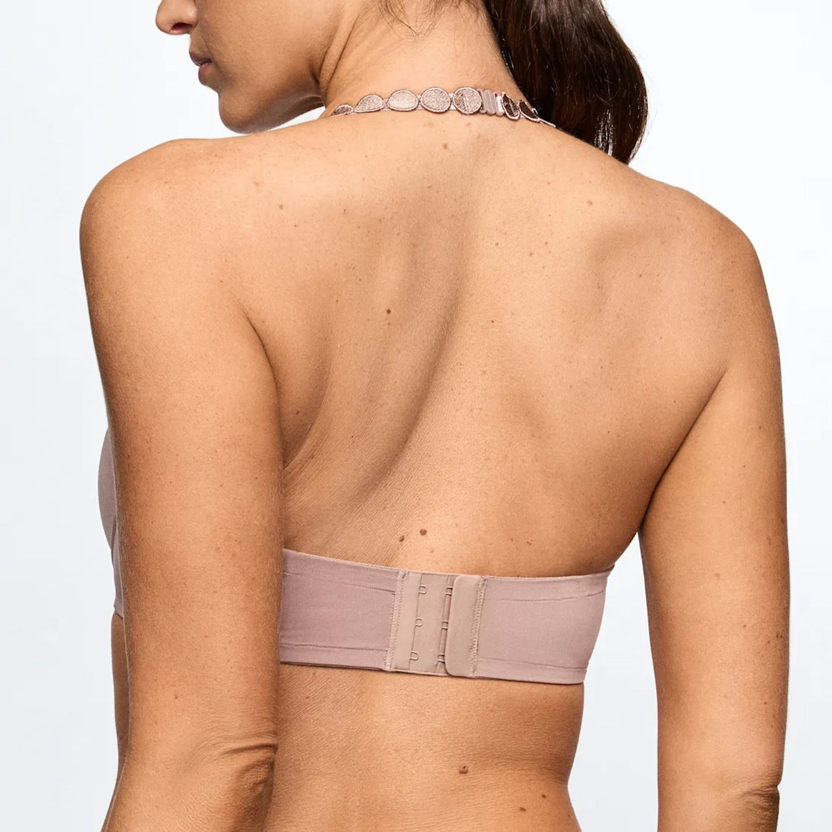 Back view of a woman wearing a strapless bandeau-style bra in a muted dusty mauve color, showing the wide underband and center closure straps.