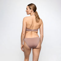 A woman shown from the back wearing a matching nude-beige bralette and high-cut bikini-style underwear set against a plain light gray studio background.