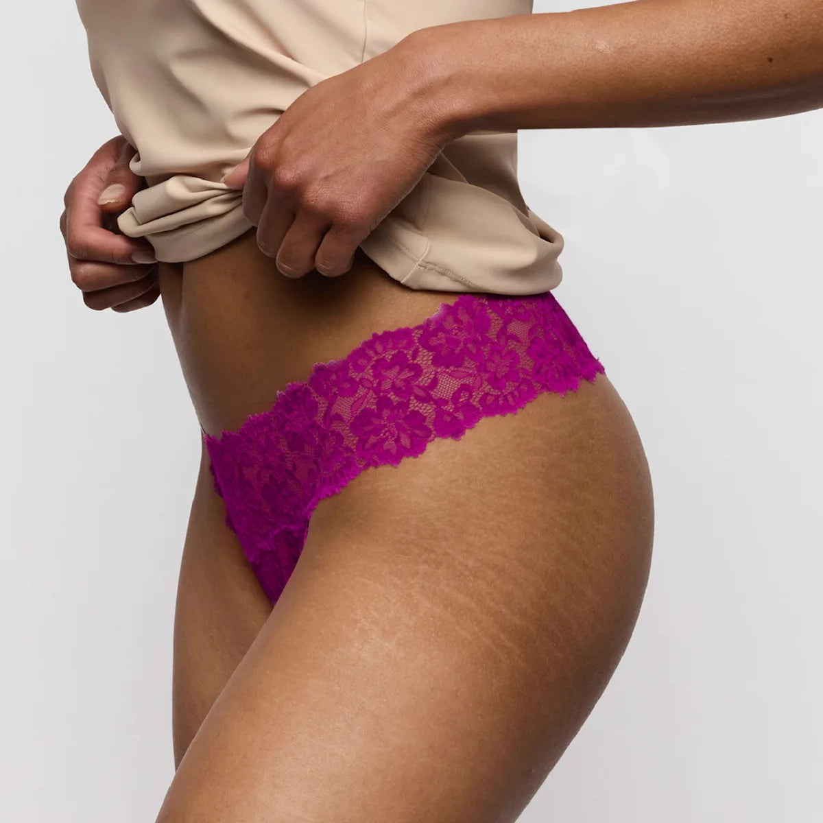 Person wearing a beige top and pink lace underwear against a plain background