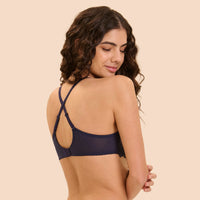 A woman with long, wavy brown hair is shown from the back wearing a navy blue bra. The bra features thin, crisscrossing shoulder straps and a sheer mesh back panel.