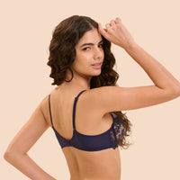 A woman modeling a navy blue lace-trimmed underwire bra, shown from the back against a solid light beige background.